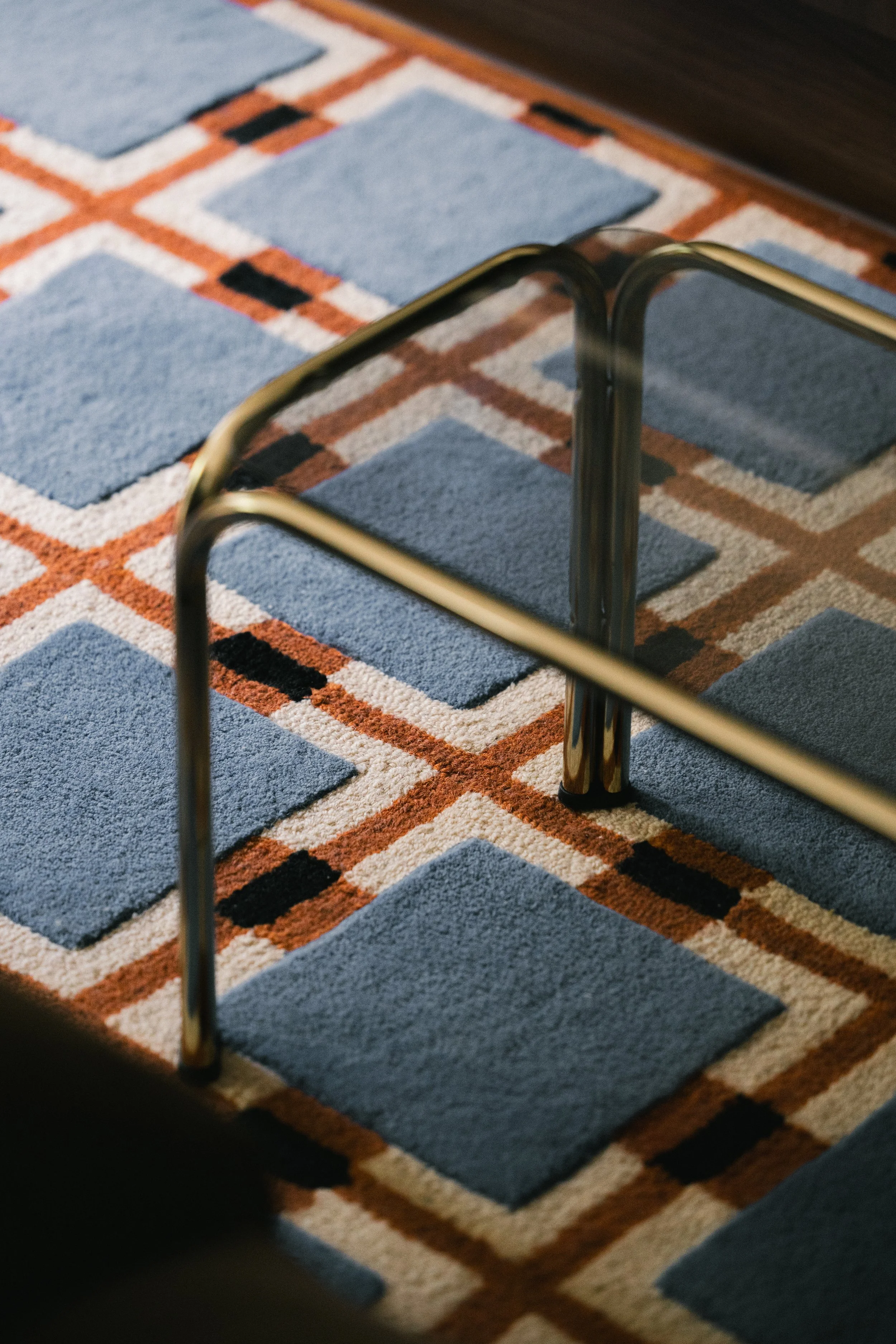 Close-up view of a metallic chair leg on a patterned blue and orange rug.