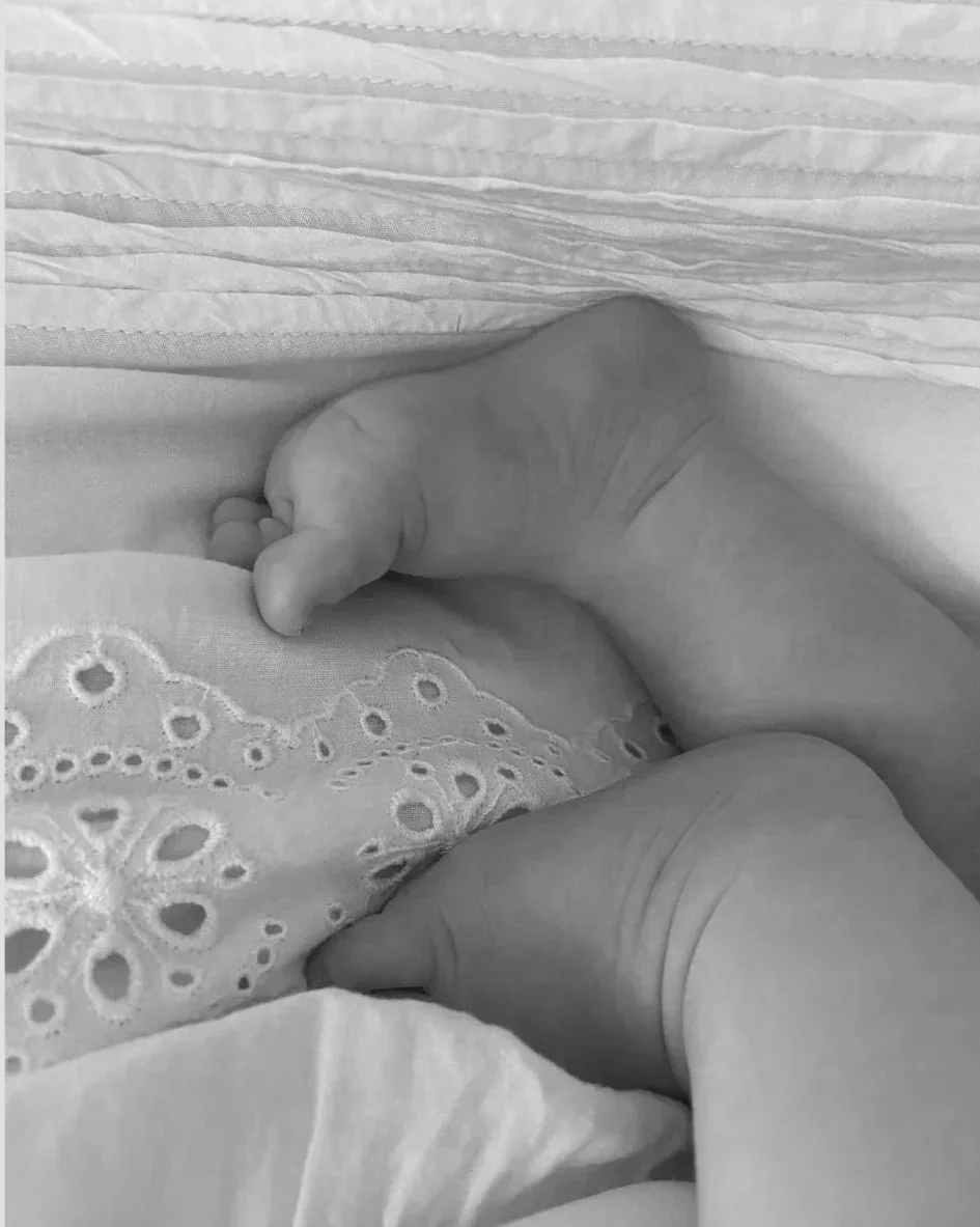 Close-up of a newborn baby's hand holding an adult's finger, lying on embroidered bedding.
