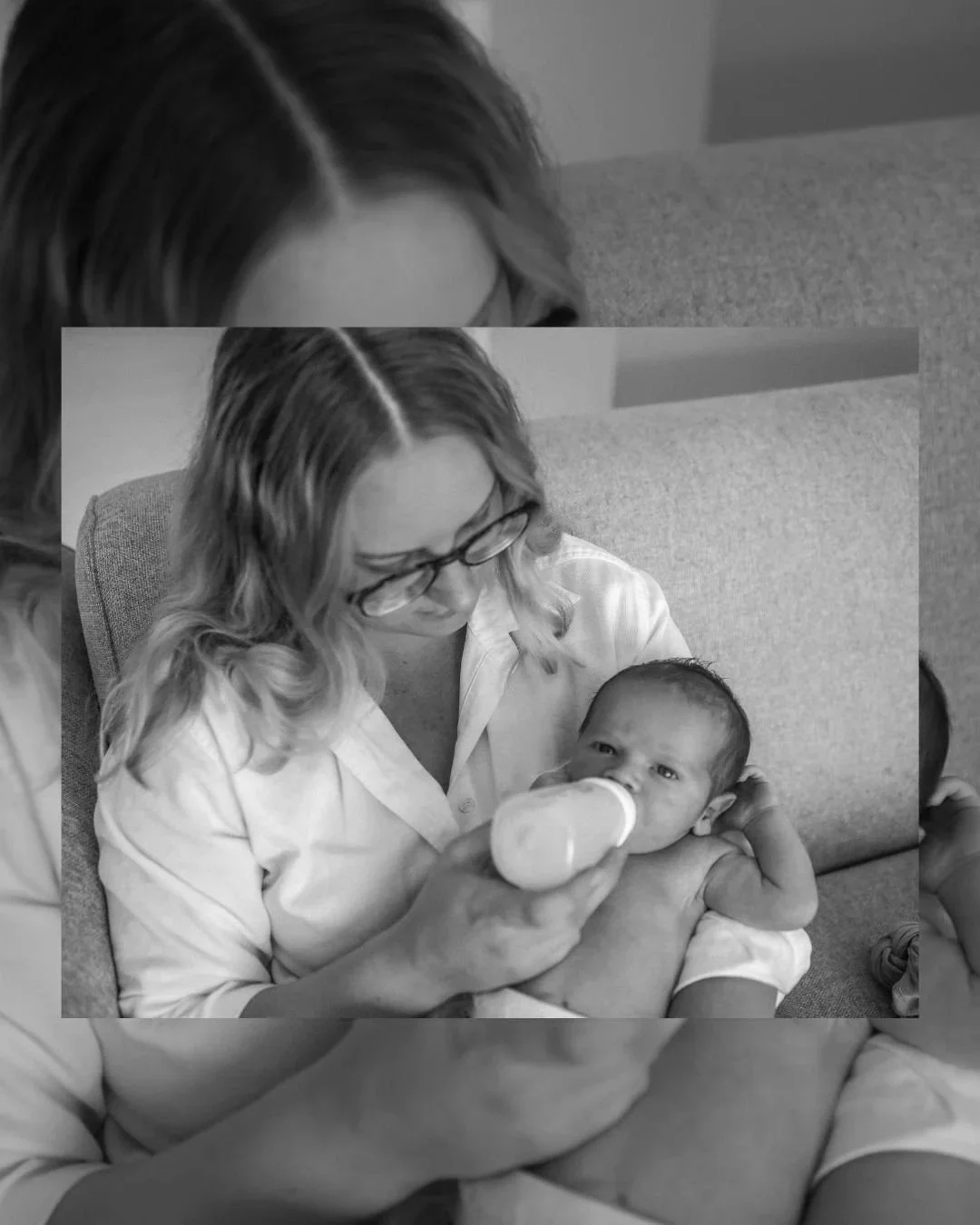 A woman with glasses feeds a newborn baby with a bottle while sitting on a couch.