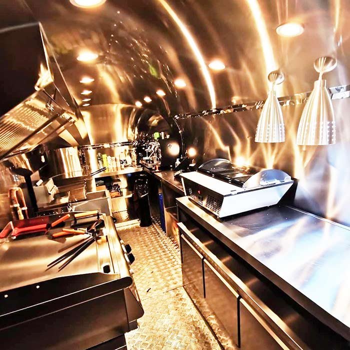 A compact, stainless steel kitchen with cooking appliances, utensils, and hanging lights, designed in a sleek, modern style.