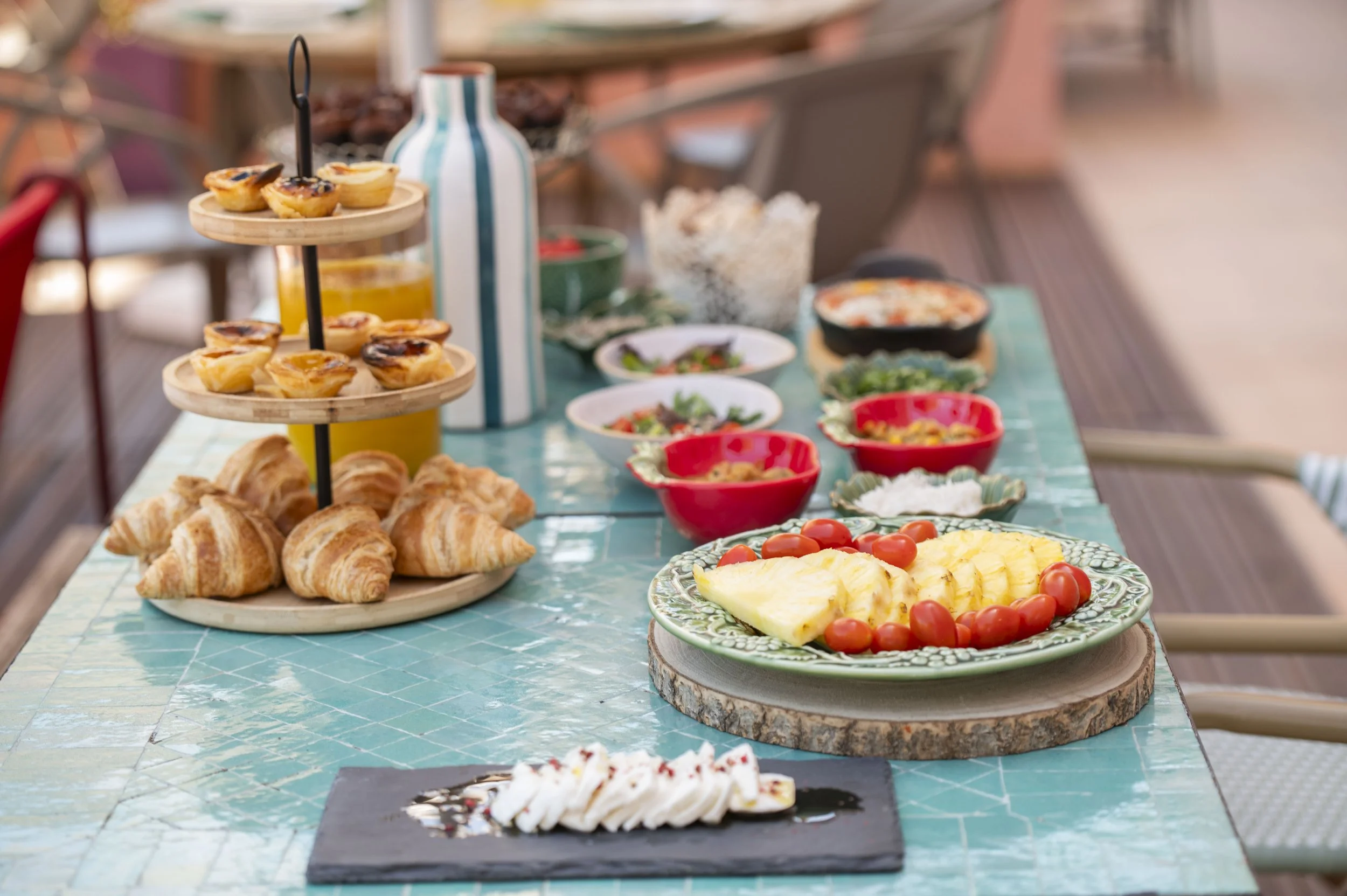 Mesa de café da manhã com pratos variados, incluindo croissants, uma torta de batata, saladas, frutas, tomates, queijo e um bolo com cobertura branca