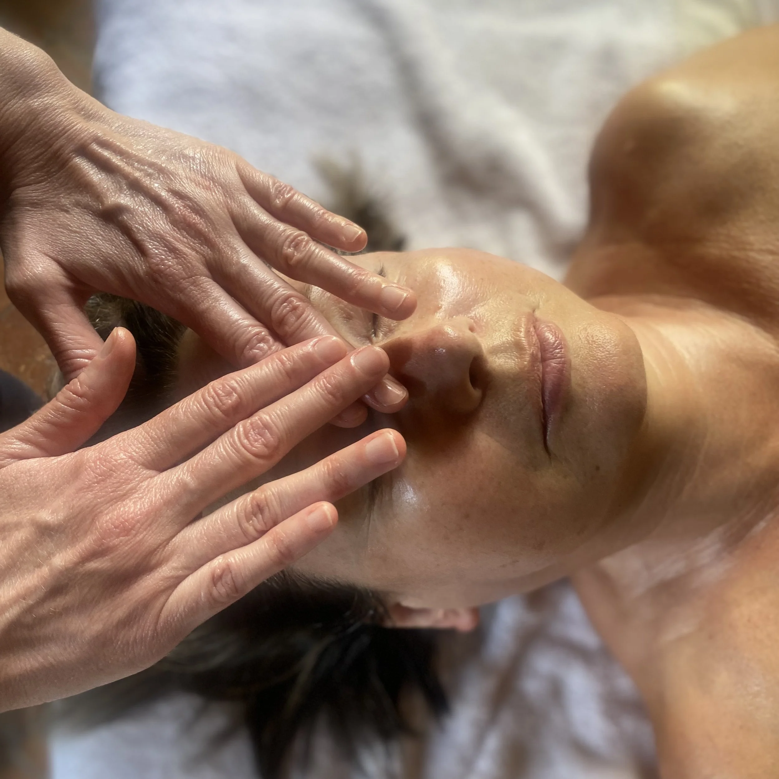 Une personne recevant un massage facialiste et un soin de la peau, la main de l'esthéticienne touche délicatement le visage de la cliente.
