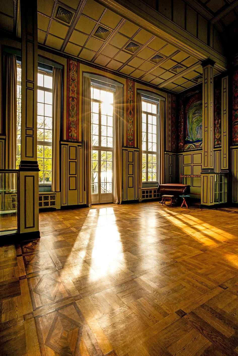 Ein sonnendurchflossener, elegant dekorierter Raum mit hohen Fenstern, Holzparkettboden und alten Wandgemälden.