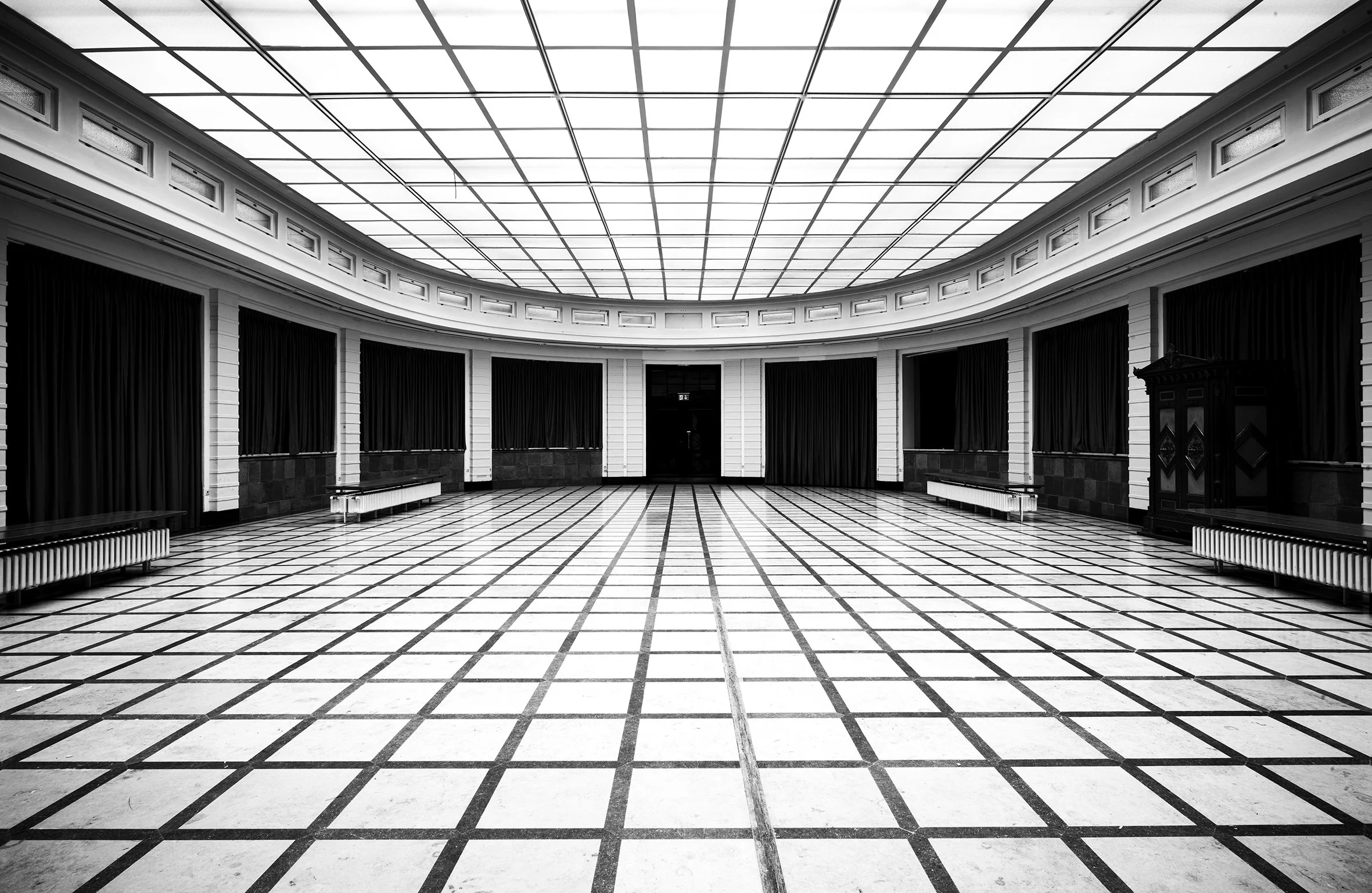 Leeres, schwarzes und weißes, quadratisches Saal mit hohen Decken, Vorhängen an den Seiten, Heizungen und einem doppelt Türen in der Mitte, in Schwarz-Weiß