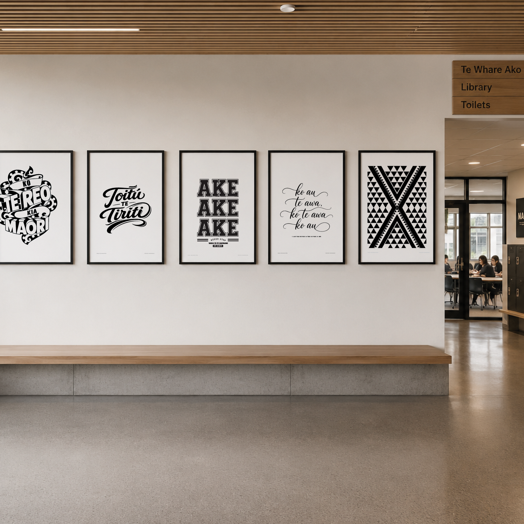 A wall with five framed black and white posters with text designs, in a modern indoor space near a corridor with people sitting at tables.