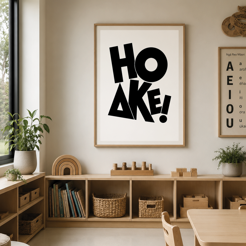 A minimalist children's playroom or learning area with a framed art print reading 'HOAKE!', wooden shelves with baskets, toys, and books, and decorative plants, natural light from a window on the left.