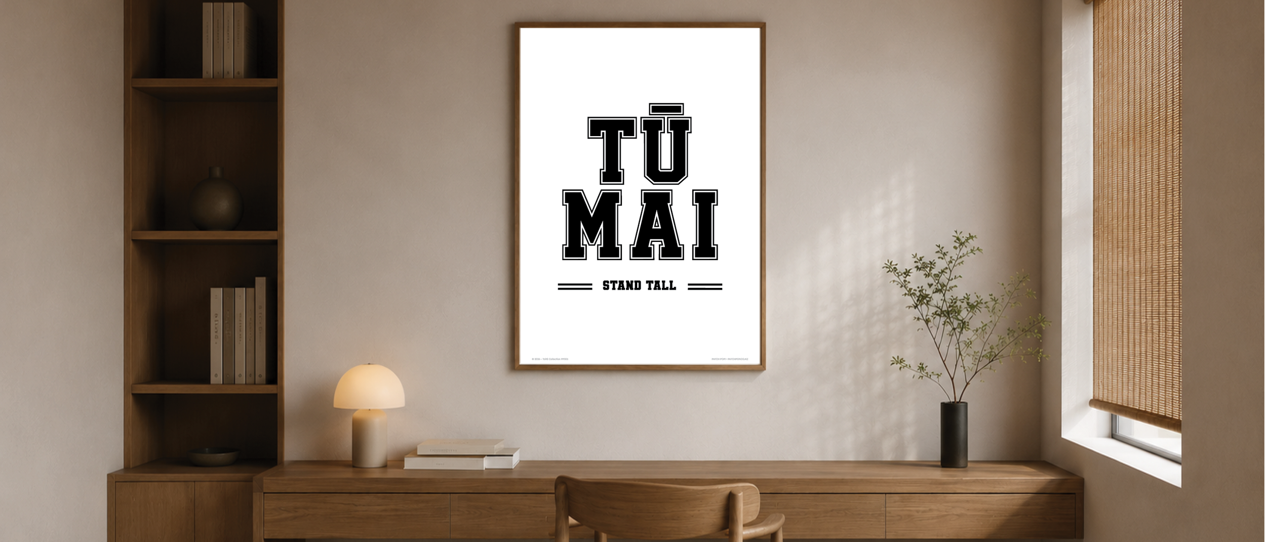 Interior room with a framed poster on the wall that has the words 'TÚ MÁI' and 'STAND TALL'. There is a wooden shelving unit with books and a vase, a small table lamp, a few stacked books, a potted plant, and a window with bamboo shade.