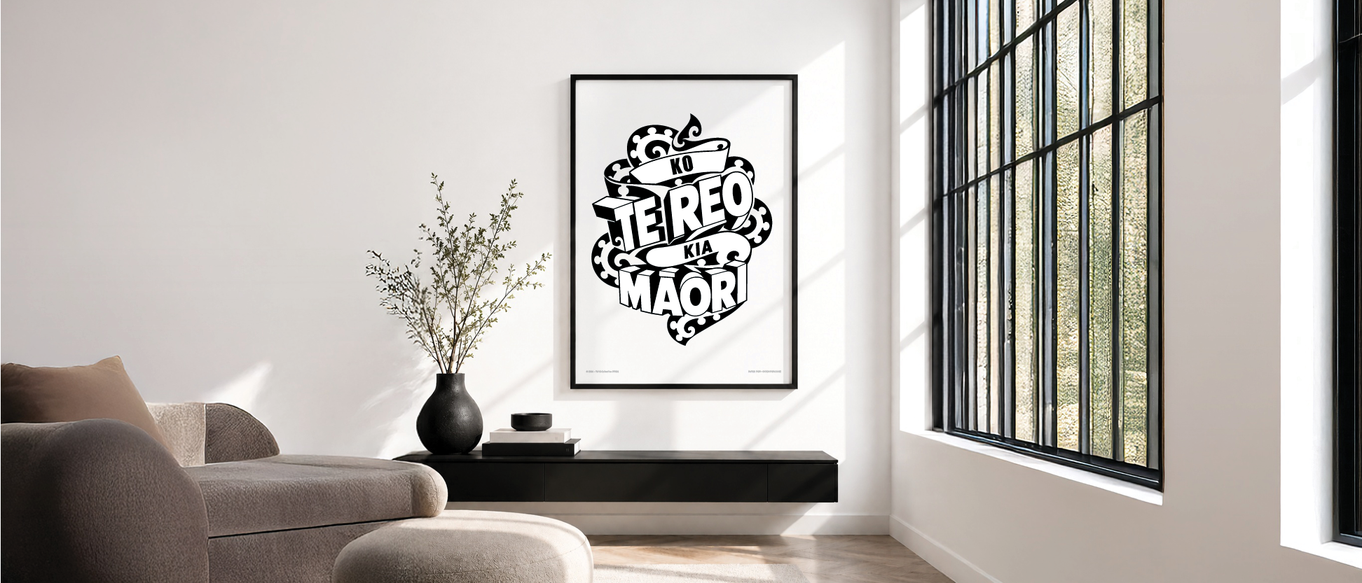 Modern living room with black and white poster, a light-colored sofa, a black vase with branches, and a window with black frame, natural light illuminating the space.
