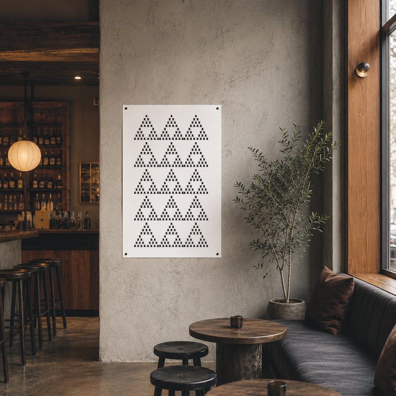 Modern cafe interior with a concrete wall, a framed art piece composed of X's arranged in rows, a window with a wooden frame, a potted plant, and a seating area with a black cushioned bench and small round wooden tables with black stools.
