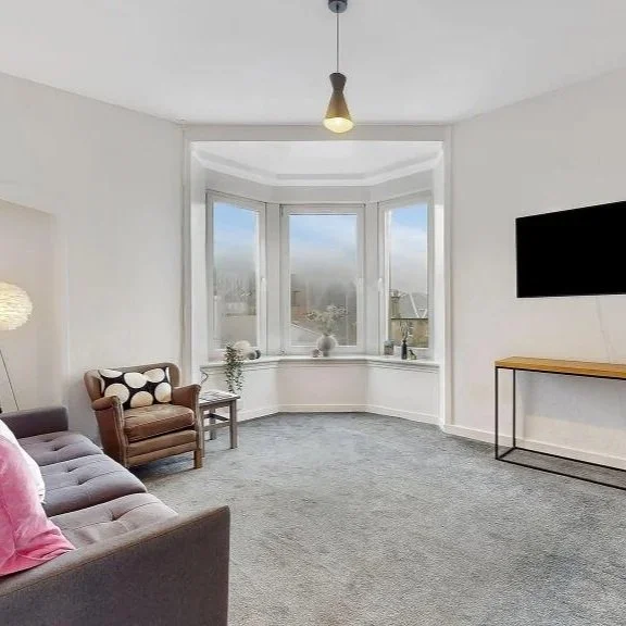 A modern house with wooden exterior walls and a large glass window, set against a mountain landscape.