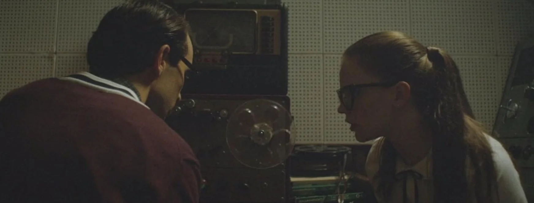 Film Still from the Film The Vast of Night (2019) with the actors Sierra McCormack and Jake Horowitz in a recording studio, surrounded by equipment including a reel to reel and soundproof walls.