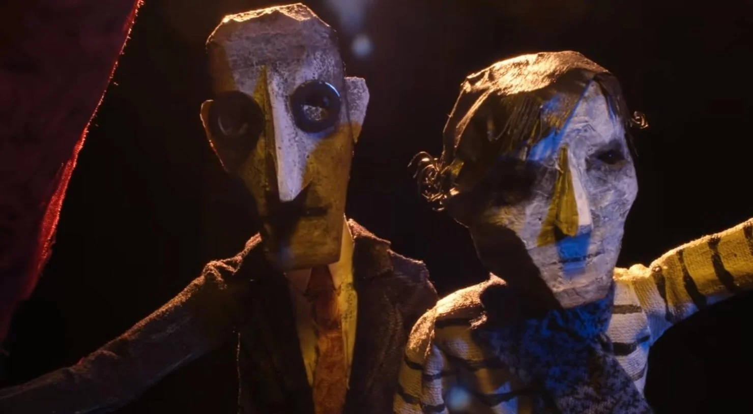 Two figures made of paper-mâché with large eyes, one with a long nose and the other with a prominent nose, illuminated by low lighting. Animated image from Edgar Wright's Documentary The Sparks Brothers (2021).