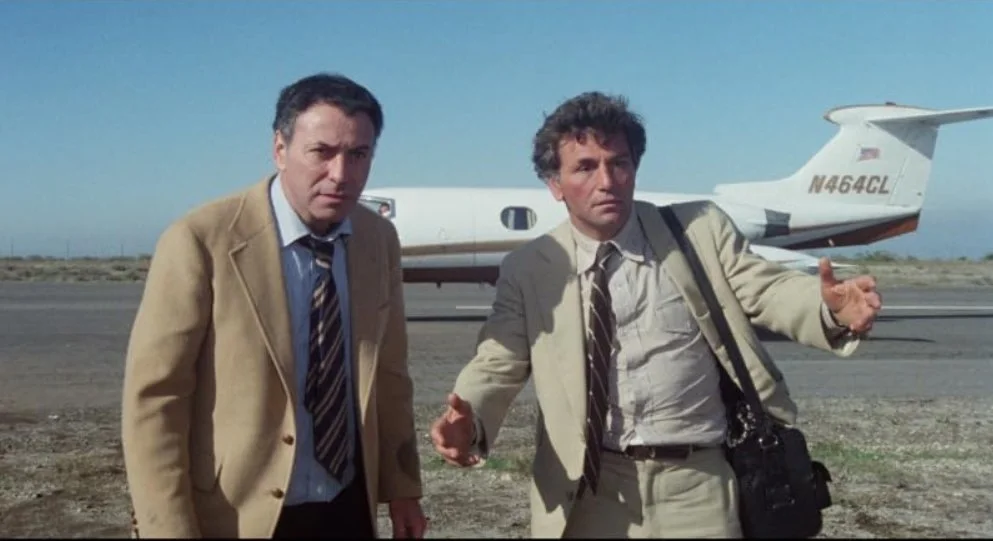 A film still from the comedy adventure film The In-Laws (1979) Featuring Peter Falk and Alan Arkin, standing on an airfield with a small passenger plane behind them.