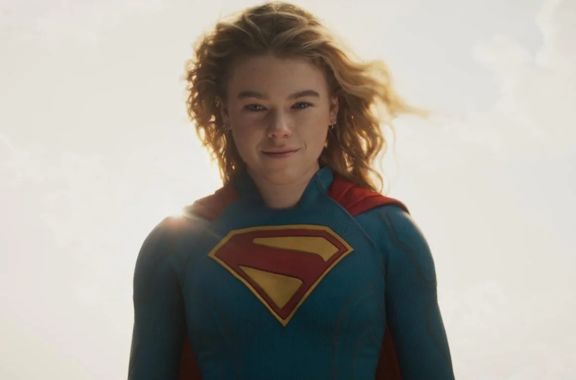 A still from the film Supergirl (2026) starring Milly Alcock dressed as Supergirl flying with the yellow sun behind her.