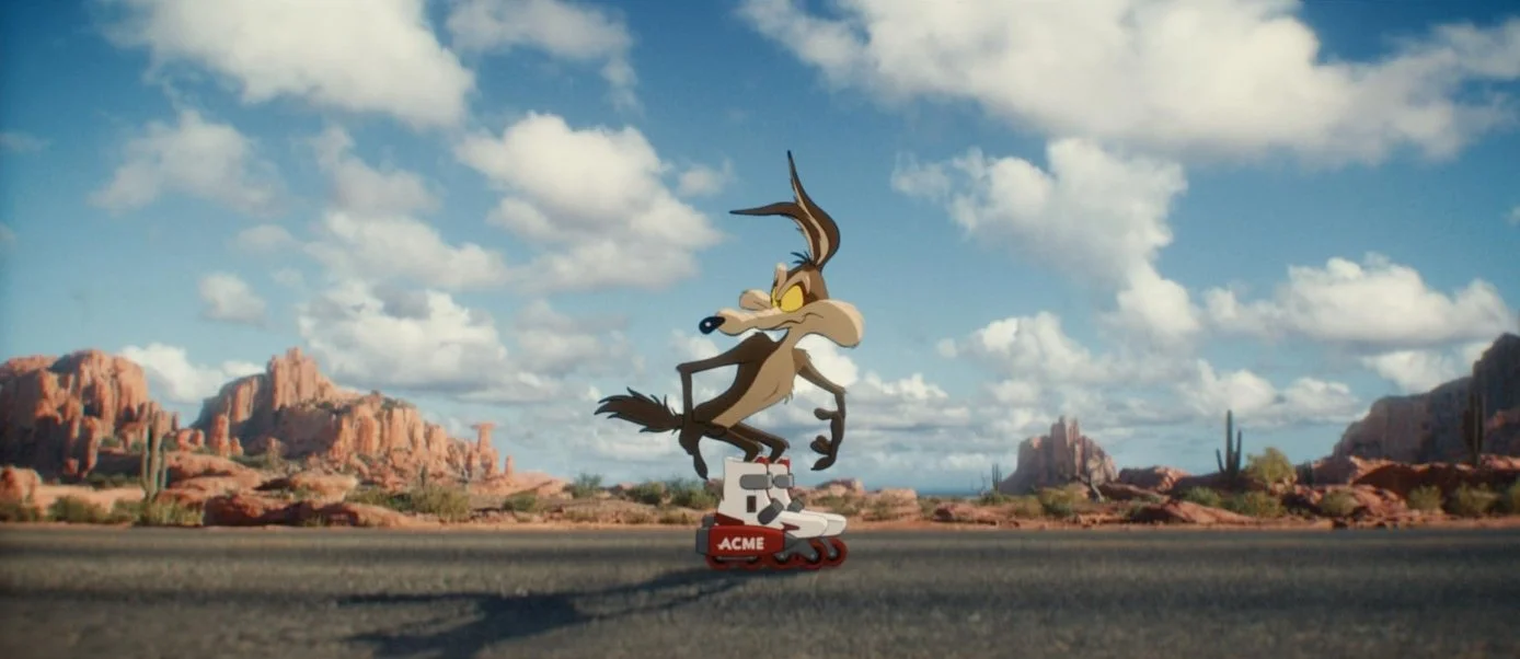 Animated image of Wile E. Coyote riding roller skates in a desert landscape with rock formations and cacti, under a partly cloudy sky. This is a Still from the 2026 film Coyote vs. Acme, starring john Cena and Will Forte.