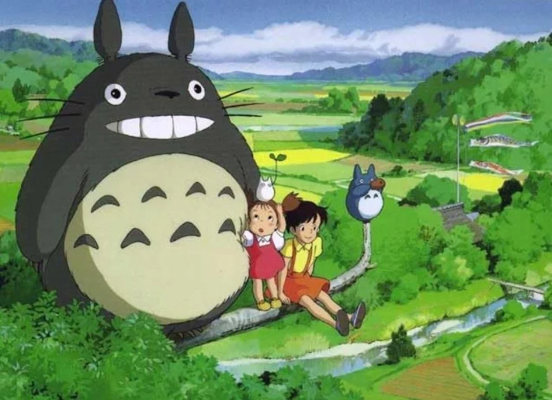 Animated scene from film My Neighbor Totoro (1988) with two children sitting on a tree branch, surrounded by lush green landscape, large Totoro character behind them.