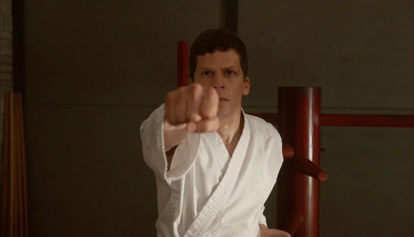 A man in a martial arts uniform practicing a punch in a dojo. A still from the 2019 film The Art of Self-Defense directed by Riley Stearns and starring Jesse Eisenberg, Alessandro Nivola and Imogen Poots.