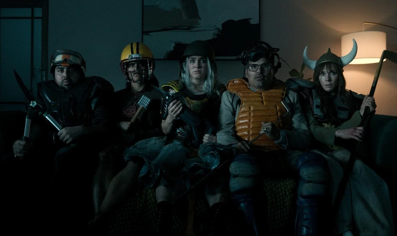 Five costumed people in medieval and fantasy armor sit together on a couch in a dimly lit room. Good Luck, Have Fun, Don't Die (2026) directed by Gore Verbinski and starring Sam Rockwell, Juno Temple and Haley Lu Richardson.