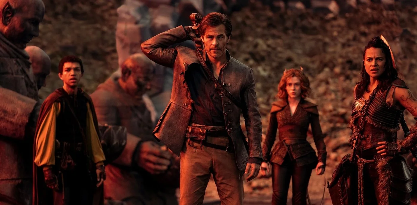 A film still from the family adventure film Dungeons & Dragons: Honour Among Thieves (2023) featuring Chris Pine, Justice Smith, Michelle Rodriguez and Sophia Lillis. A man is reaching for a lute on his back, a female teifling is behind him.