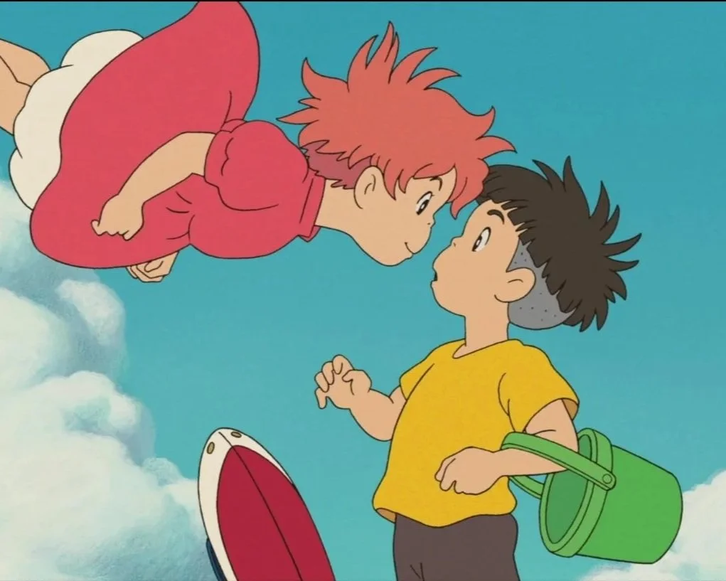 A still from the 2008 film by Studio Ghibli, Ponyo. A floating girl with ginger hair and a red dress leans towards a boy with spiky black hair, who is holding a green bucket, with a blue sky and clouds in the background.