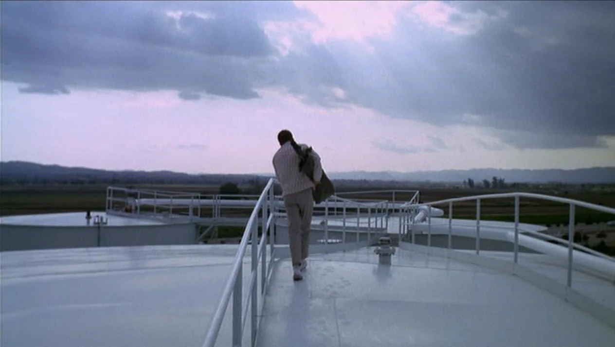 A man with a backpack walking on the roof of a tall building with a cloudy sky in the background. This is a scene from Peter Bogdanovich's debut 1968 film Targets, starring Boris Karloff.