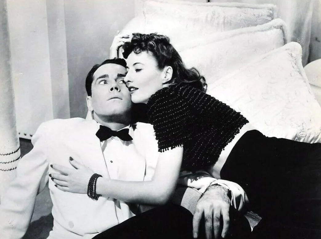A black and white film still from the rom-com The Lady Eve (1941) featuring Henry Fonda and Barbara Stanwyck. A woman embraces a man who looks worried they are both dressed in evening attire.