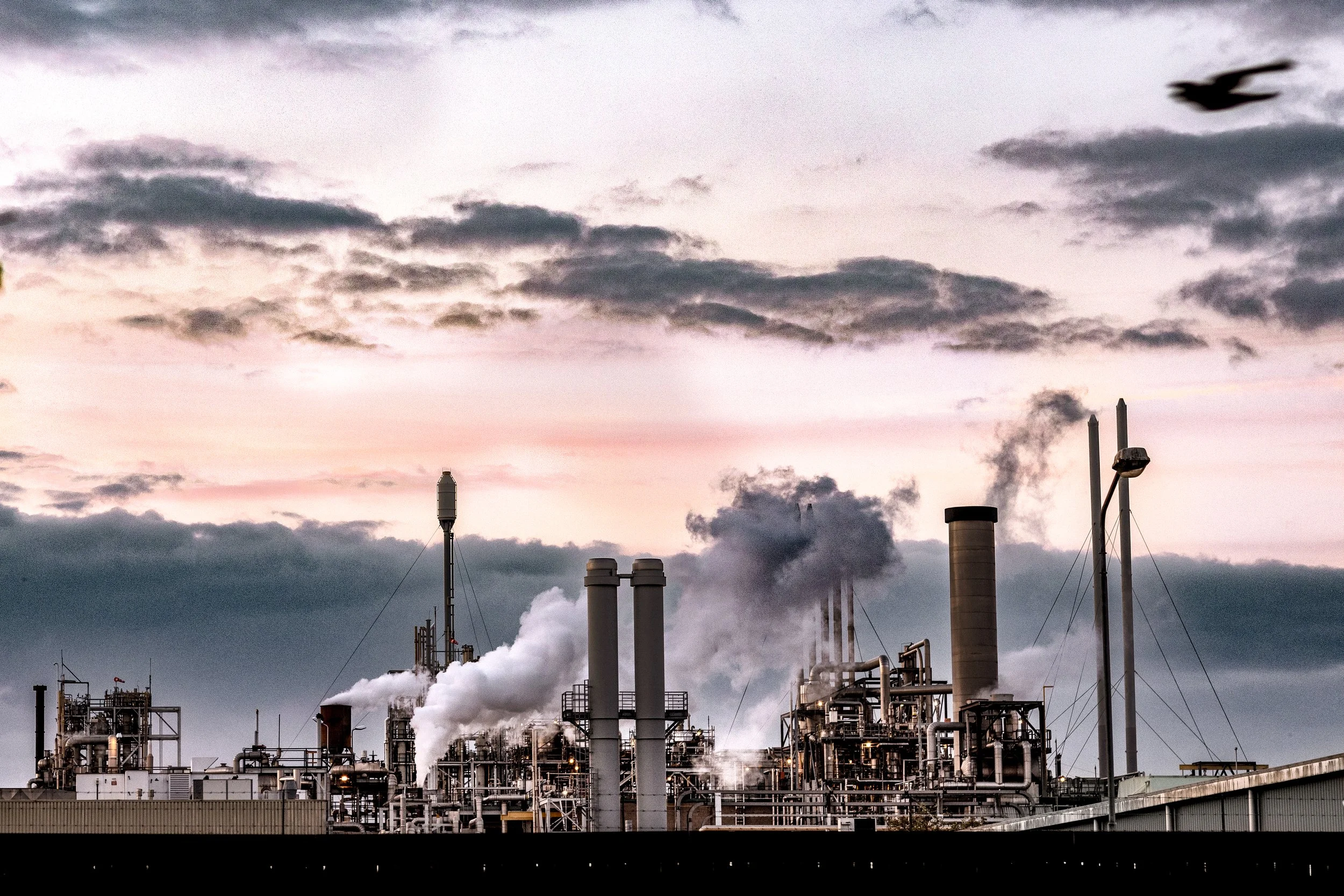Industriegebouw met rook en dampen die uit de schoorstenen komt, onder een bewolkte hemel tijdens schemering.