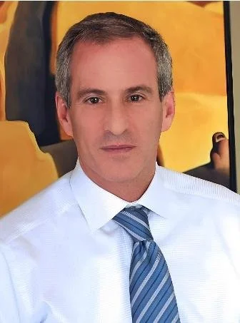 Man in wit overhemd en blauwe stropdas, zittend in een voertuig met gele en zwarte stoelen.