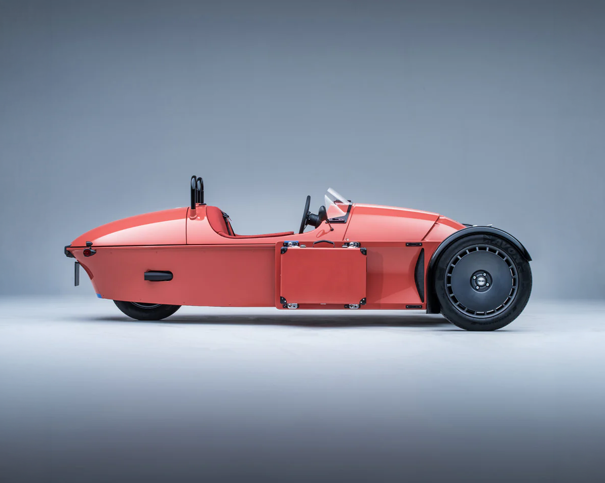 Side view of a sleek, red, futuristic, single-seater hover motorcycle with a streamlined body, two small rear wheels and a large front wheel, set against a plain gray background.