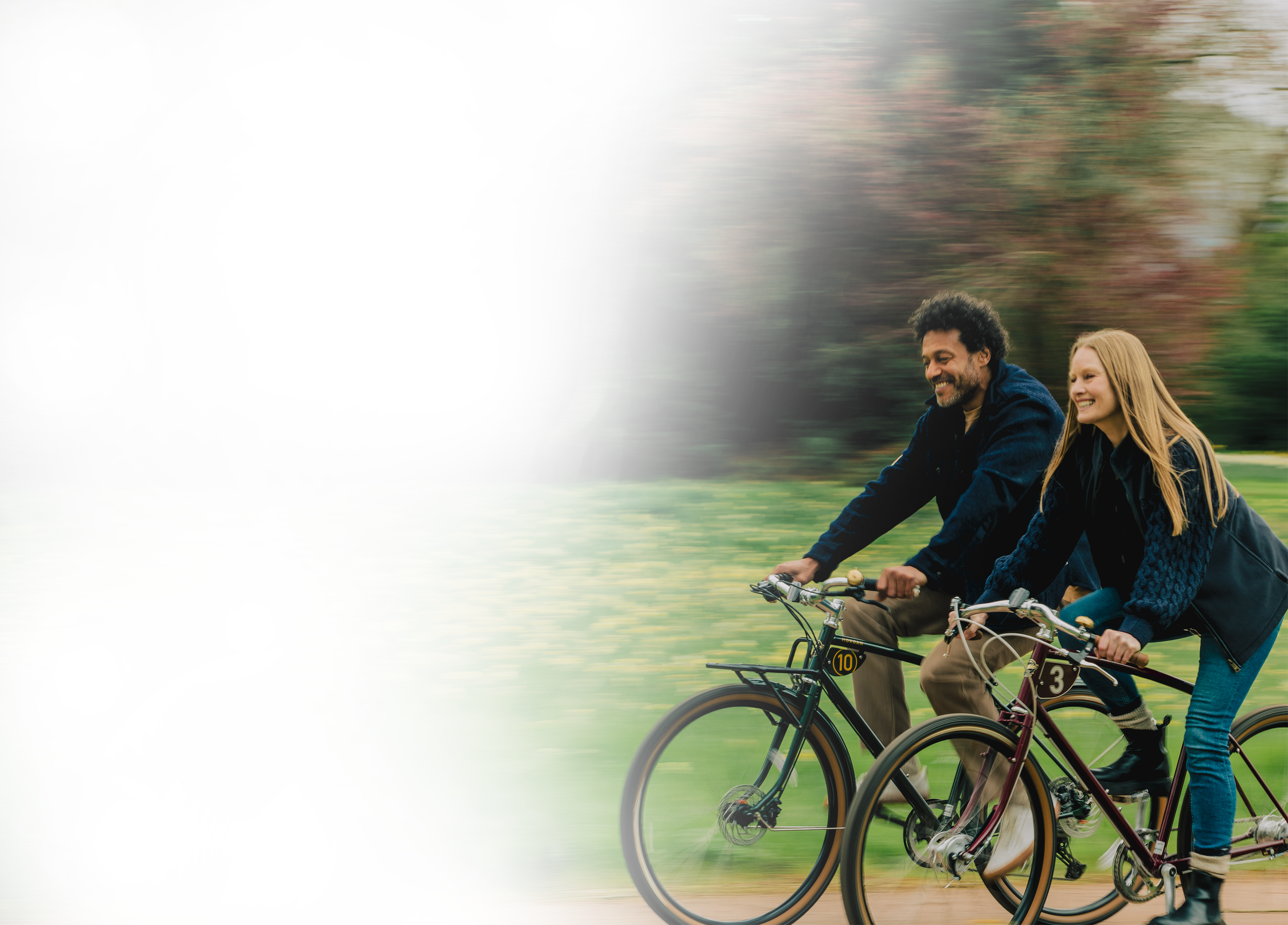 A man and a woman riding bicycles in a park with trees, smiling and enjoying the outdoors.