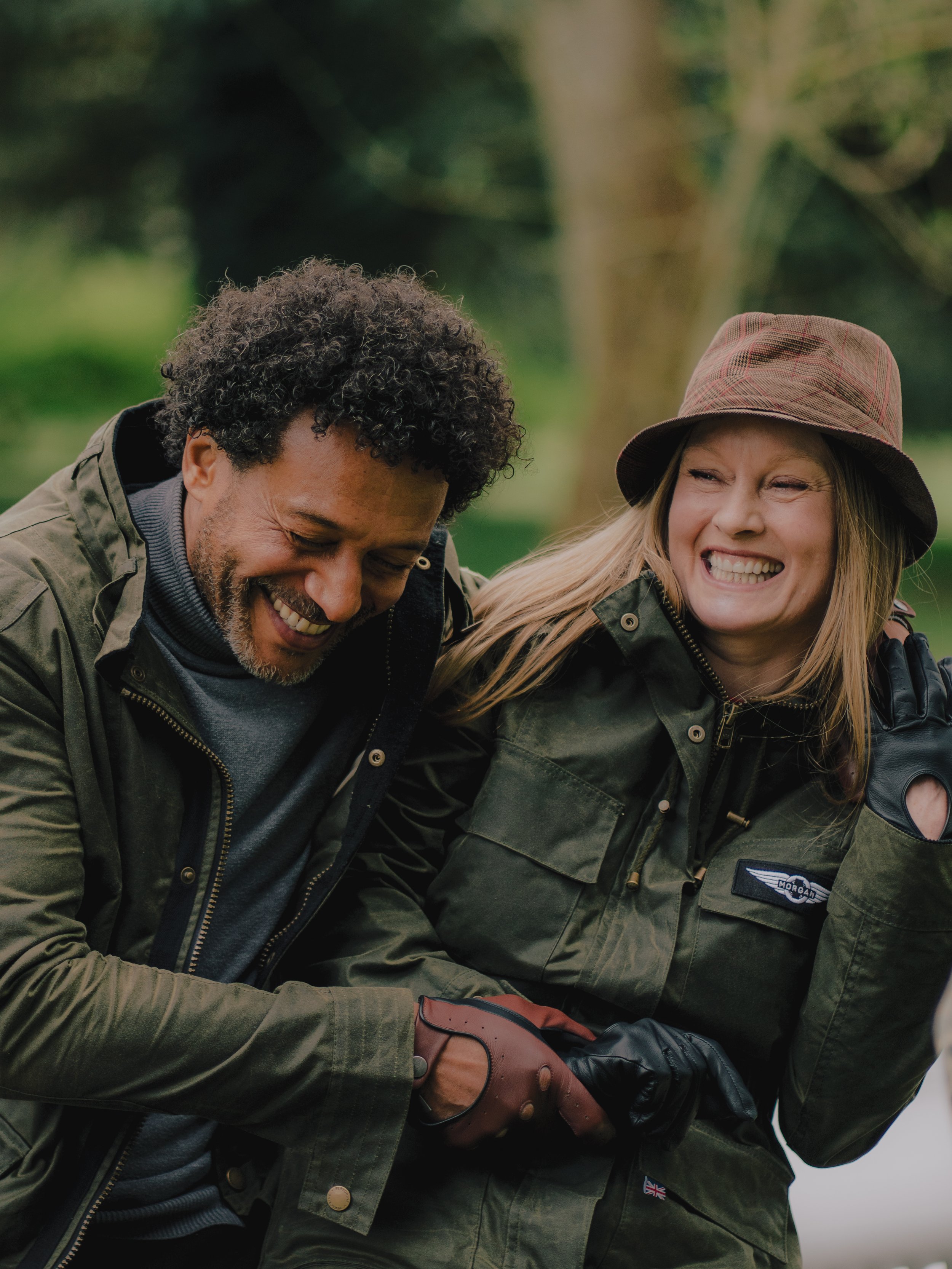 Two people smiling and laughing, engaged in a friendly group activity outdoors, wearing green jackets.