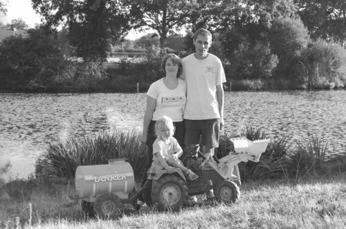 Photo de Jean-Paul et Sabrina avec leur fille sur un tracteur à pédales dans les années 2000.