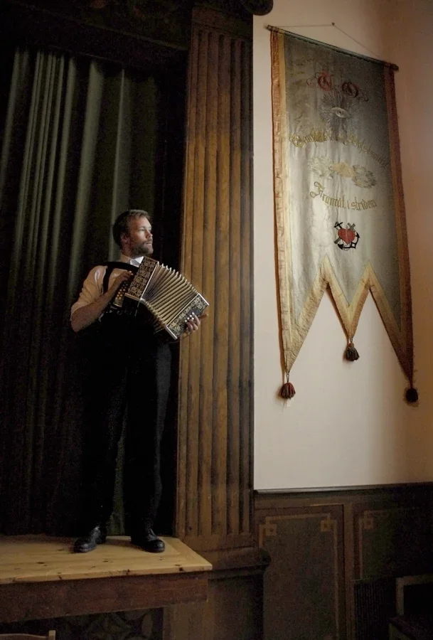 En man står på en liten scen i en gammal byggnad och spelar dragspel.