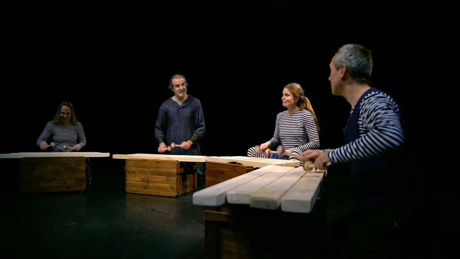 Fyra personer, två kvinnor och två män, spelar marimba på en scen med svart bakgrund. Alla håller i träklubbor och är klädda i randiga tröjor.