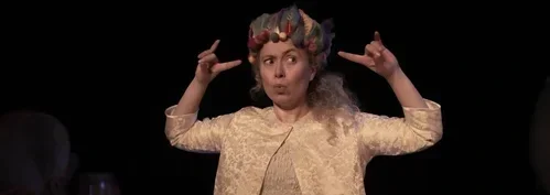 Kvinna med en fantasifull hårstyling som ser ut som horn, gör ett rockhandtecken med båda händerna.