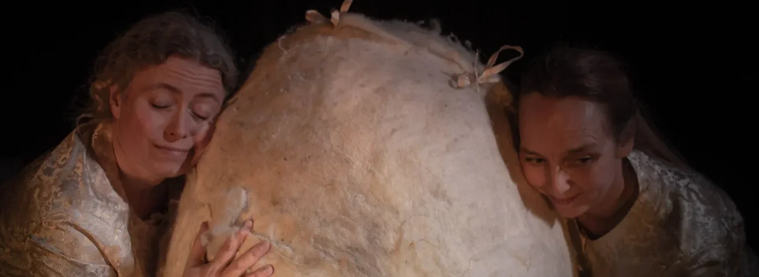 Två personer omfamnar ett stort ljusgult bröd, de håller om det och ser känslosamma ut.