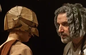 En man med grått hår och skägg samt en person med ett unikt, norrländskt, traditionellt hår och huvudbonad.