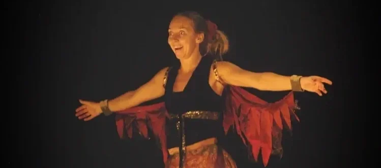 En kvinna som dansar, iklädd en färgglad kostym med utbredda armar.