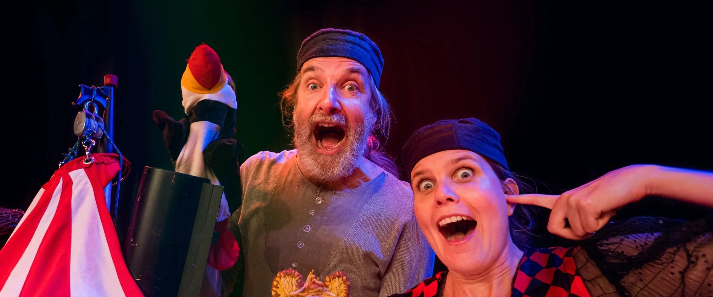 Två personer i piratkostymer med en handdocka, som ser förvånade ut, i en teater eller scenshow.