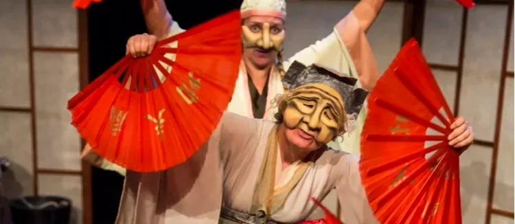 Två personer i japanska masker och traditionella kläder som håller röda parasoller.