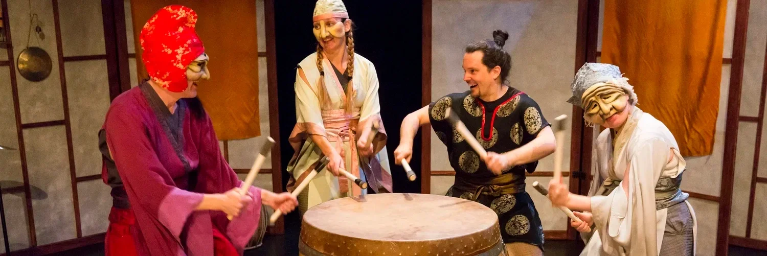 Fyra personer i traditionella japanska masker och kläder som spelar på en trumma.