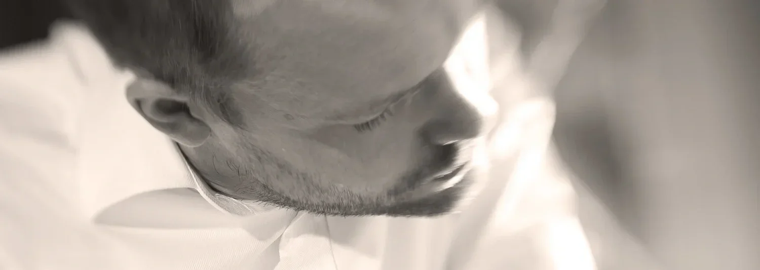 En närbild av en persons ansikte, troligtvis en man, som tittar neråt och är delvis skuggad.