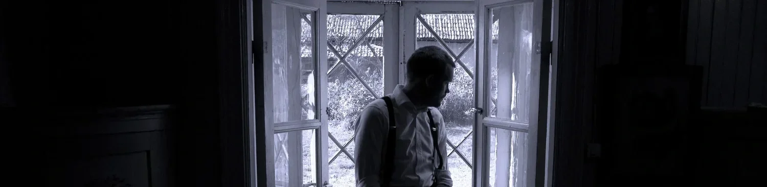 En man står vid ett öppet fönster, silhuett mot ljuset, inomhusmiljö.