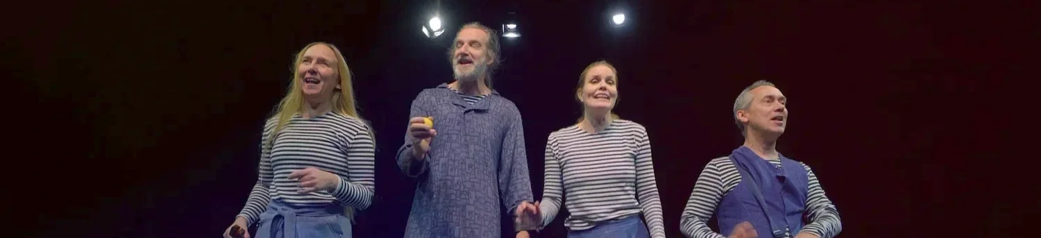 Fyra personer står på en scen, alla bär randiga tröjor och ler, med ett mörkt bakgrund och några ljus ovanför.