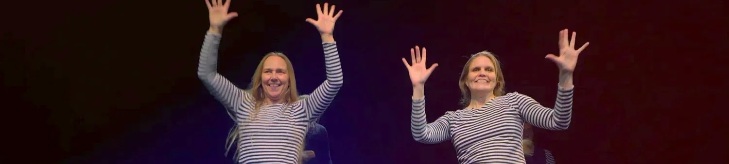 Två kvinnor i randiga tröjor som ler och vinkar med händerna mot kameran.