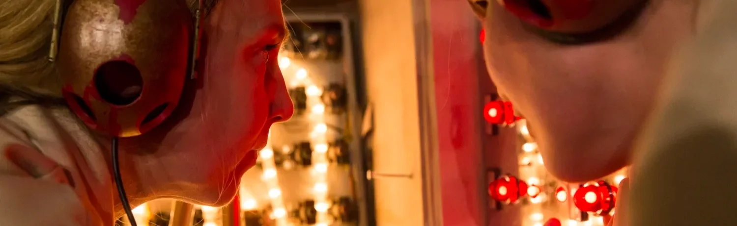 En närbild av en kvinna som granskar ett föremål, bärandes hörlurar och omgiven av röda lampor.