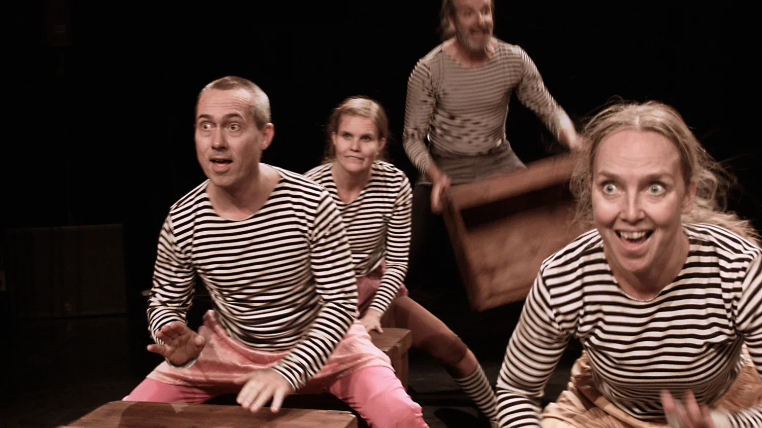 Fyra personer i randiga tröjor på en scen, engagerade i en teaterföreställning.