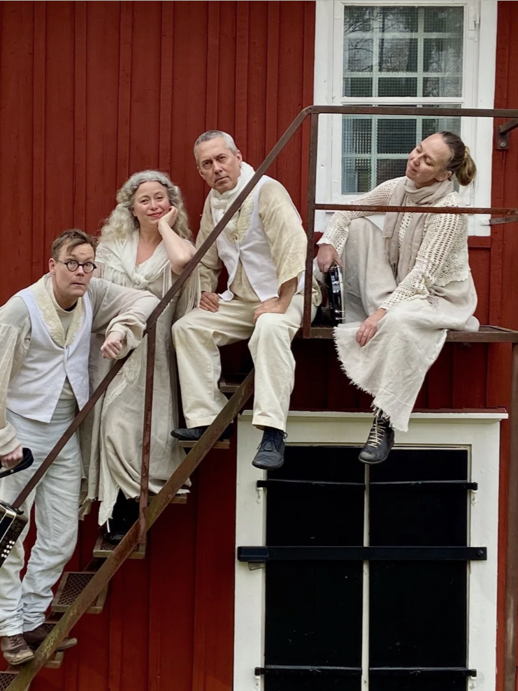 Fem personer står och sitter på en brant trappa framför en röd, trävägg.