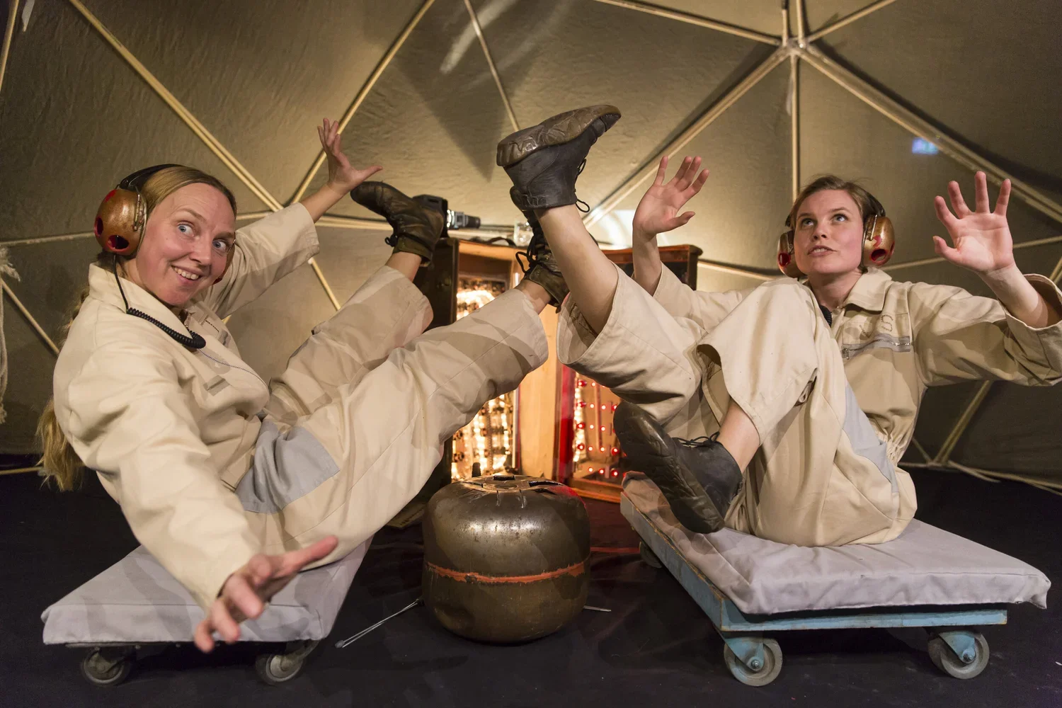 Två kvinnor i flygplansdräkter ligger på golvet och leker att de flyger, med deras fötter i luften och armarna utsträckta.