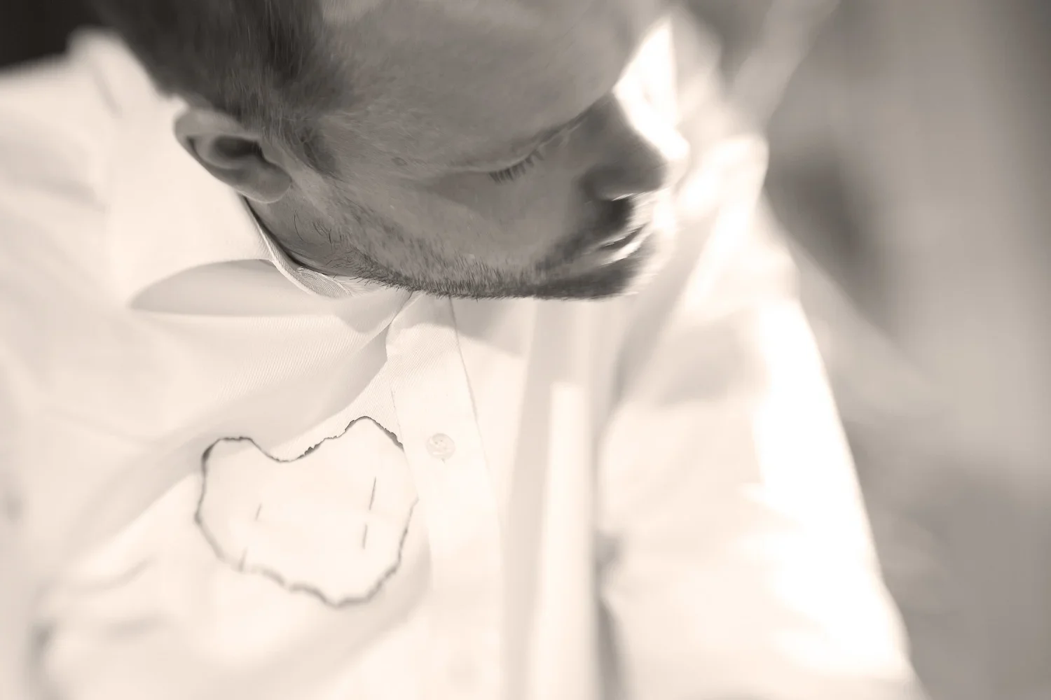 Närbild av en mans ansikte, nedsänkt, iförd en vit skjorta med en hjärtformad broderad detalj.